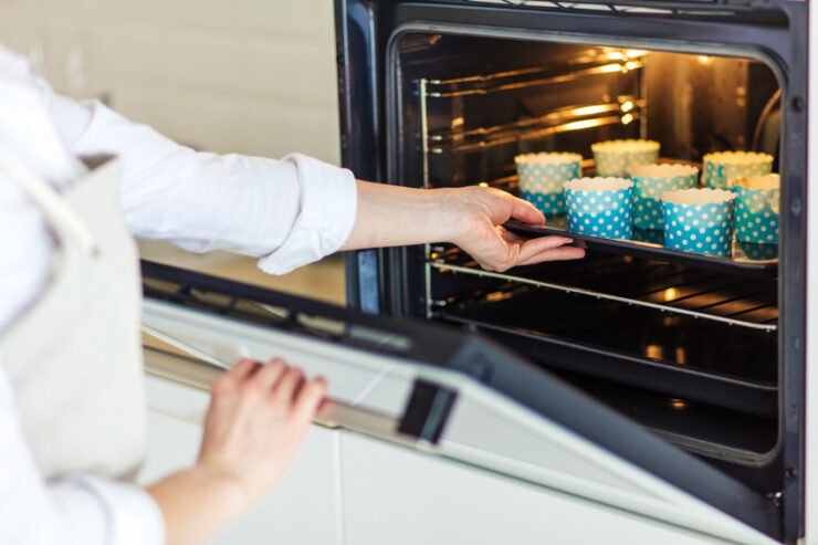 woman's hands putting the baking sheet with cupcakes in the oven